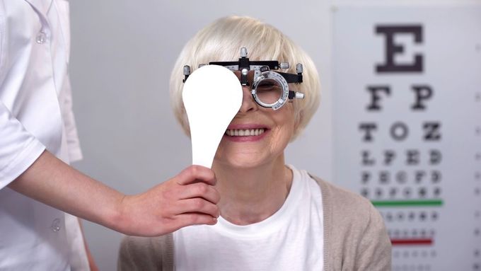 Optician closing one eye to smiling elderly woman in phoropter, perfect vision
