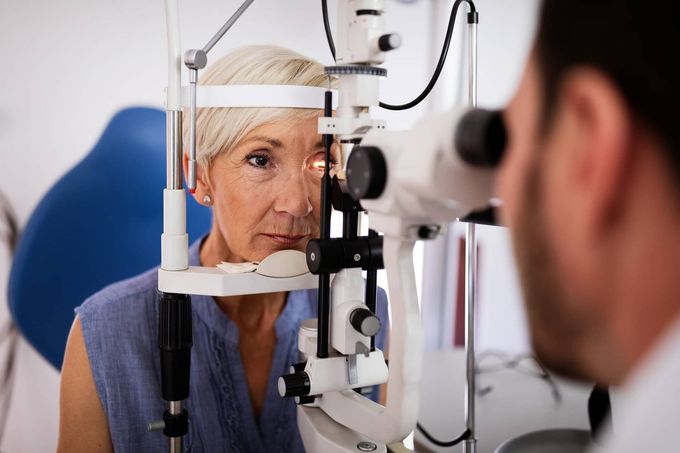 Middle-aged woman getting eye exam with a slit lamp, doctor looking in her eye.