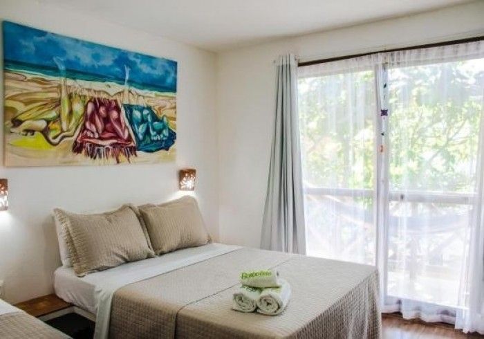 Quarto com cama de casal queen-size, obras de arte e porta de correr para uma varanda. Toalhas na cama.