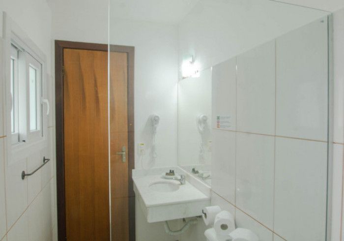 Banheiro com porta de madeira, pia branca, espelho e vaso sanitário.