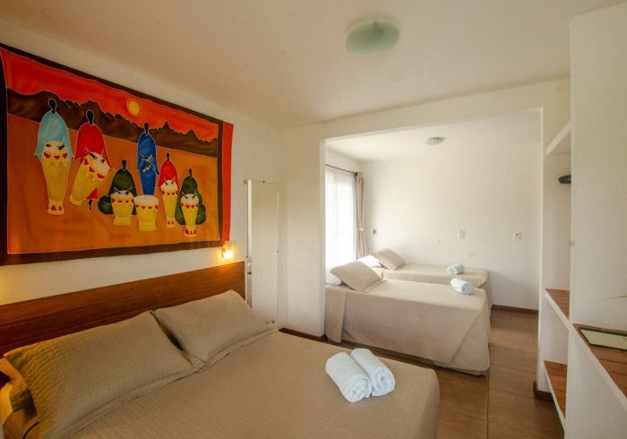 Quarto com cama de casal, três camas de solteiro, obras de arte coloridas e uma prateleira embutida.