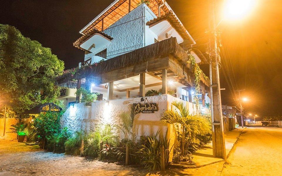 Hotel à noite com paredes brancas, detalhes em madeira e varandas iluminadas ao longo de uma rua.