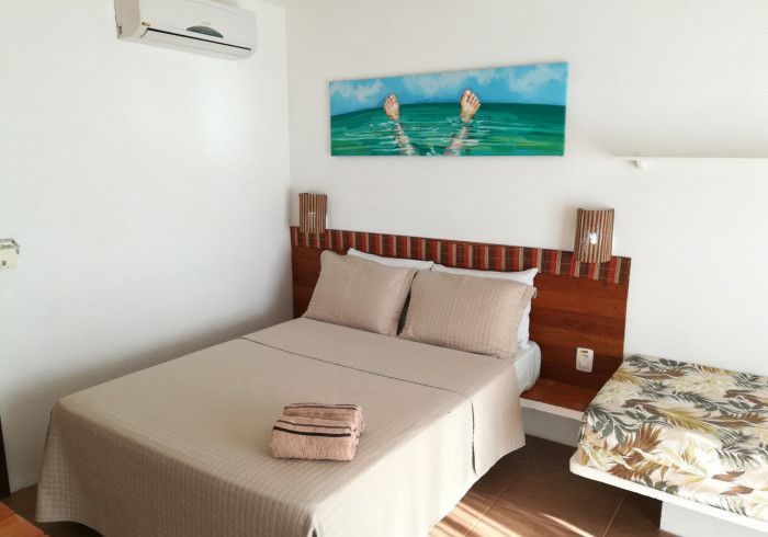 Quarto com cama de casal, obra de arte representando uma pessoa na água, ar condicionado, cabeceira e mesa de cabeceira de madeira.