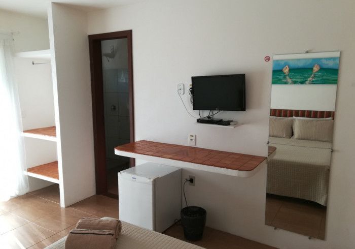 Quarto de hotel com cama, TV, frigobar, armário e espelho.