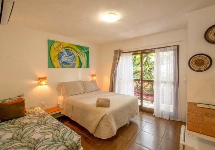 Quarto com cama, sofá-cama e porta para varanda. Quadro acima da cama e arandelas.