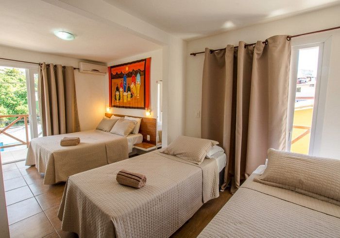 Quarto com três camas: duas de casal e uma de solteiro. Decoração de parede em tons de laranja, roupa de cama e cortinas bege.