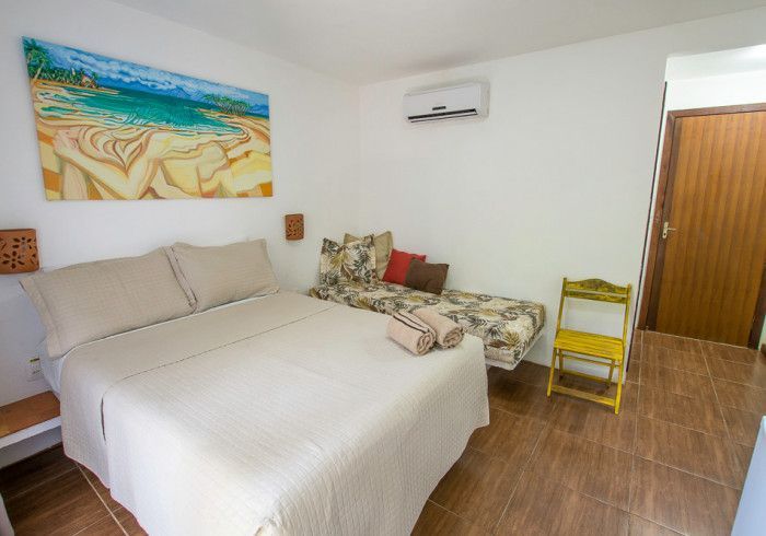 Quarto com cama de casal, sofá-cama, cadeira amarela e um quadro com tema de praia.