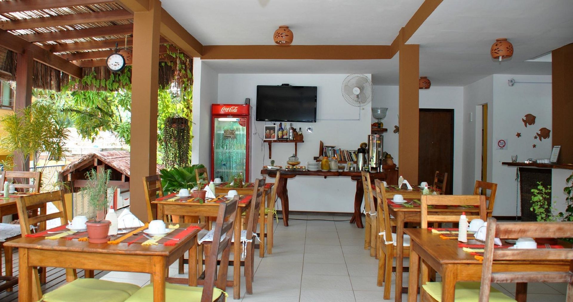 Interior do restaurante com mesas e cadeiras de madeira, um buffet e um refrigerador da Coca-Cola.