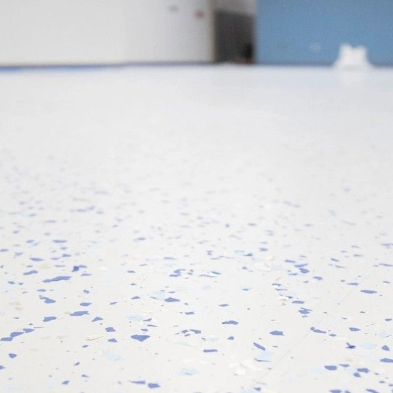 White floor with blue specks, viewed from a low angle with a blurry background of walls and a door.