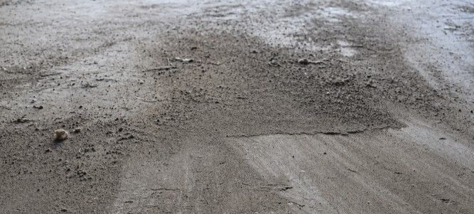 Dusty bare concrete floor in a garage showing loose surface dust and an unfinished appearance that can make the space harder to keep clean and maintain.