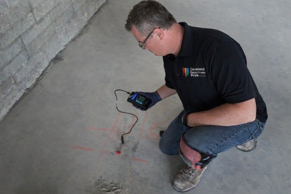 Cleveland Epoxy & Coating Pros tech kneeling on concrete floor uses a moisture detecting device to inspect a concrete floor before epoxy install