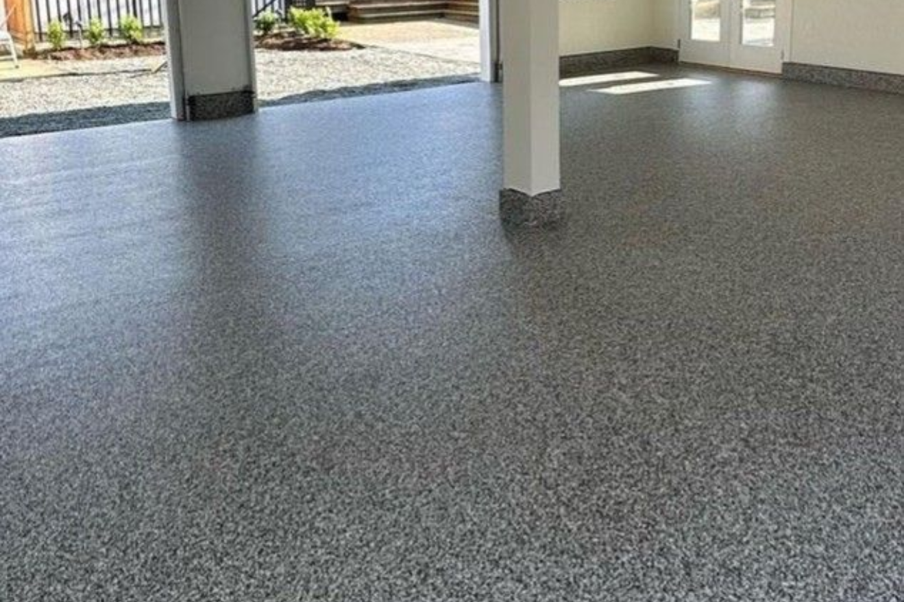 An open, brightly lit three-car garage with grey speckled epoxy flooring, white walls, and two garage door openers.