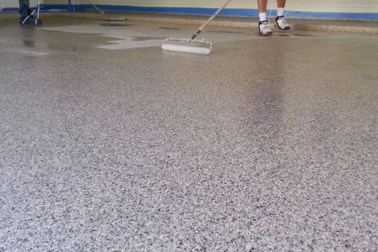 Worker smoothing a wet speckled floor with a long-handled squeegee in a room
