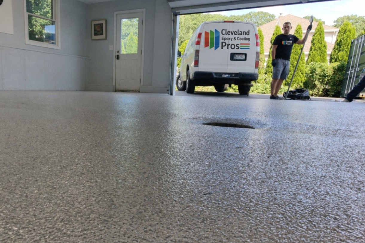 A person stands outside a garage next to a service van, looking over a newly coated, speckled grey concrete floor.