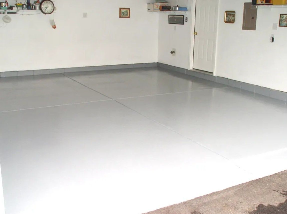 A freshly painted solid light gray epoxy garage floor with matching baseboards and white walls.
