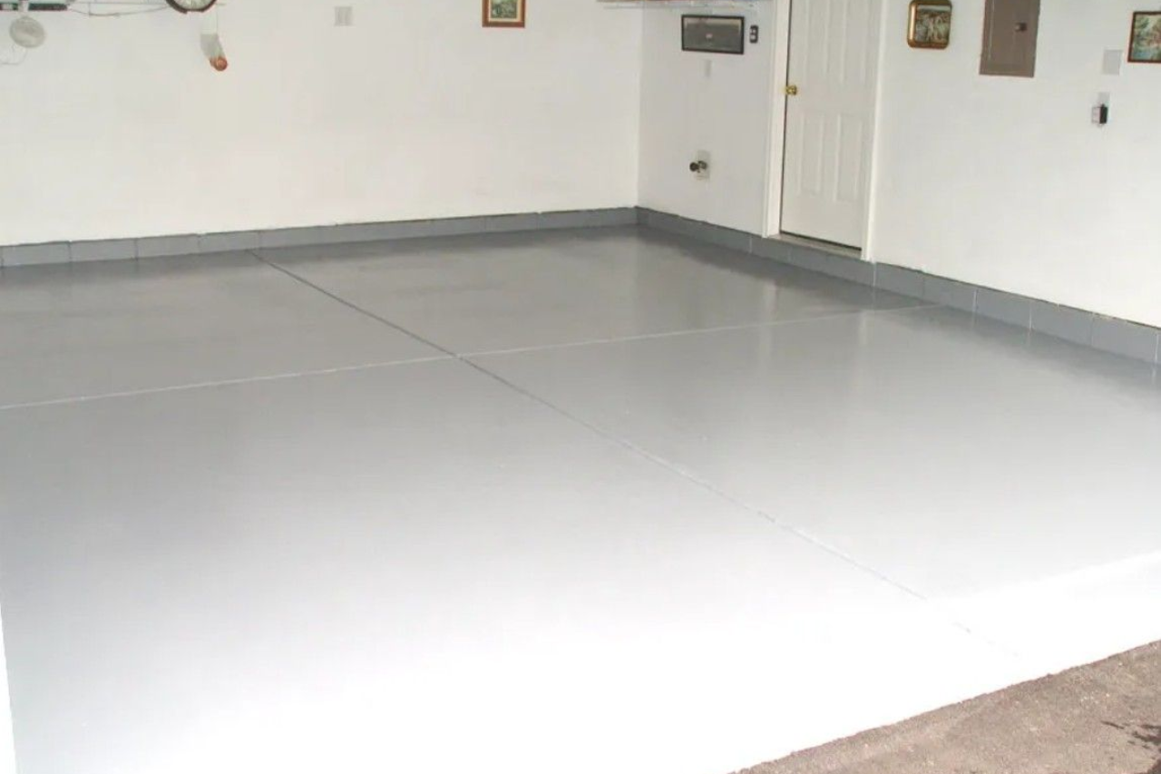 A freshly painted solid light gray epoxy garage floor with matching baseboards and white walls.