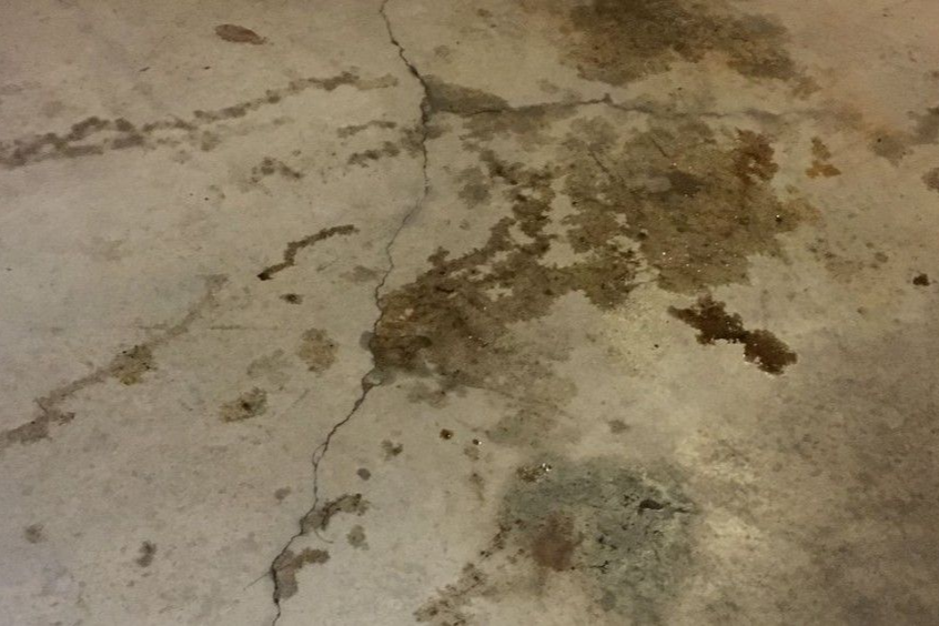 Cracked concrete floor with brown stains and a damp patch