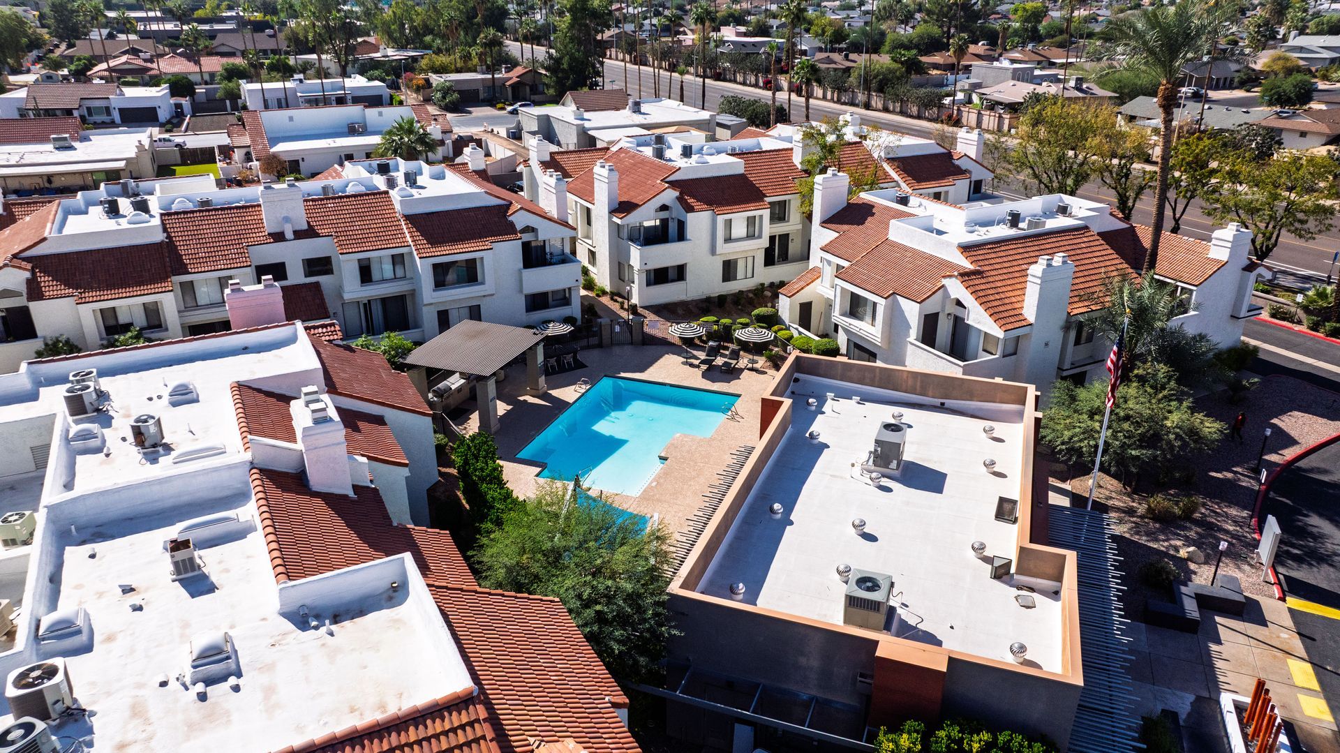 Aerial view of a complex with red-tiled roofs, white walls, and a blue swimming pool in the center.