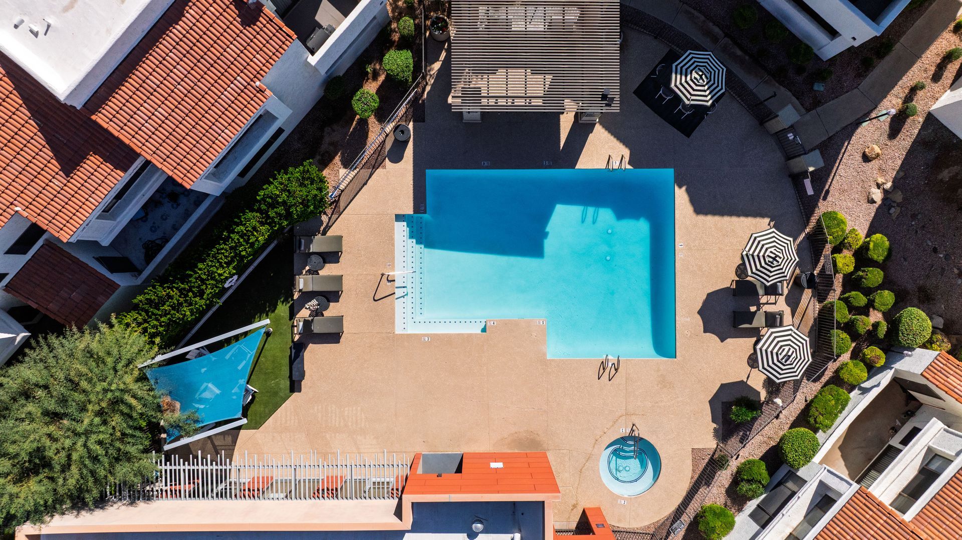 Overhead view of a swimming pool surrounded by buildings with clay tile roofs and shaded lounge areas. Live well in a welcoming pet-friendly community at Talavera Apartments.