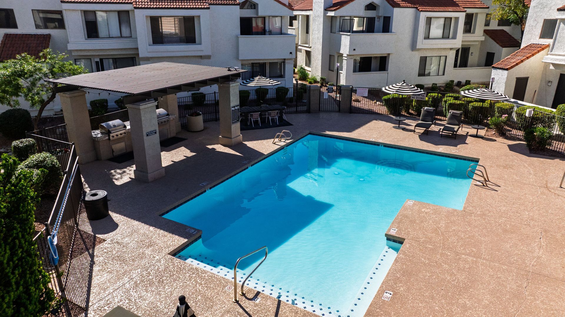 Pool and patio area surrounded by white buildings with red tile roofs. Talavera Apartments provides relaxed Tempe AZ rentals—learn more today.