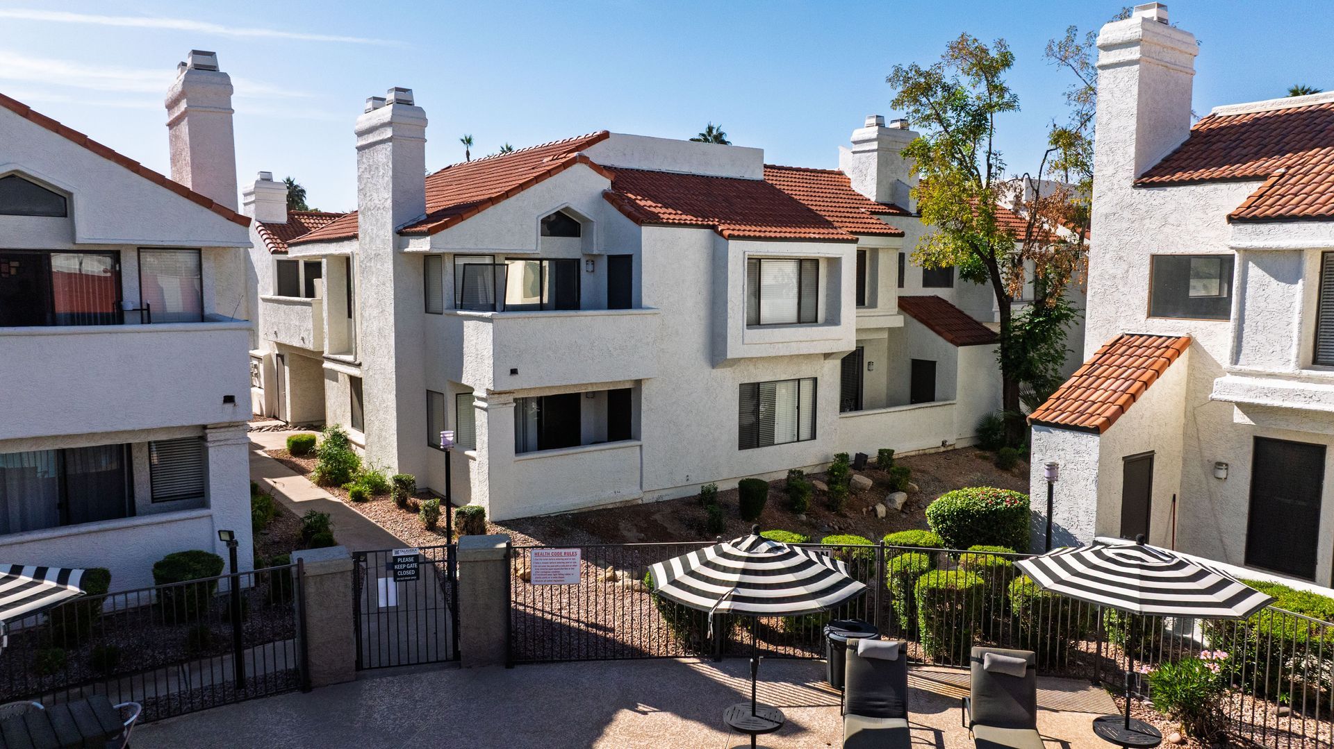 White apartment complex with orange tile roofs, outdoor pool area with umbrellas. Talavera Apartments showcases bright apartment homes in Tempe AZ—see more.