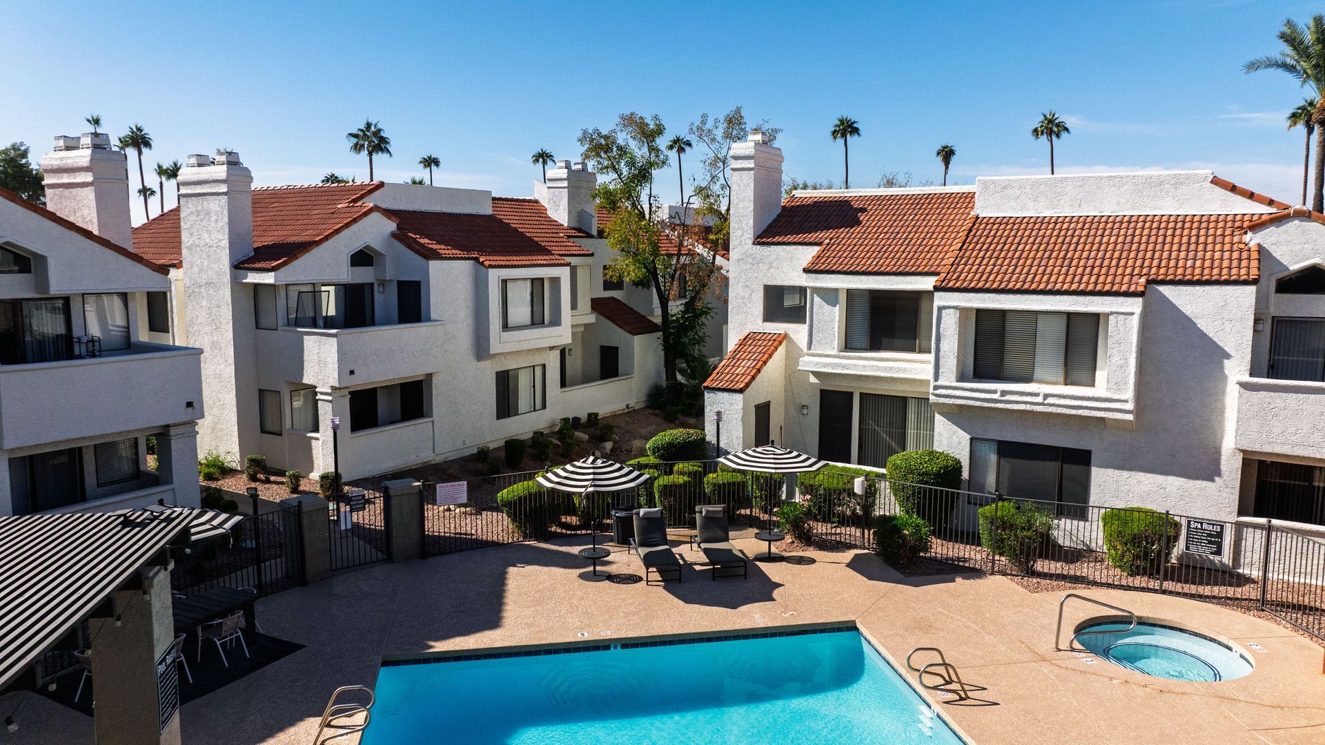 Multi-story white apartment buildings with orange tile roofs. Cars parked in front. Enjoy modern living in a pet-friendly community at Talavera Apartments.