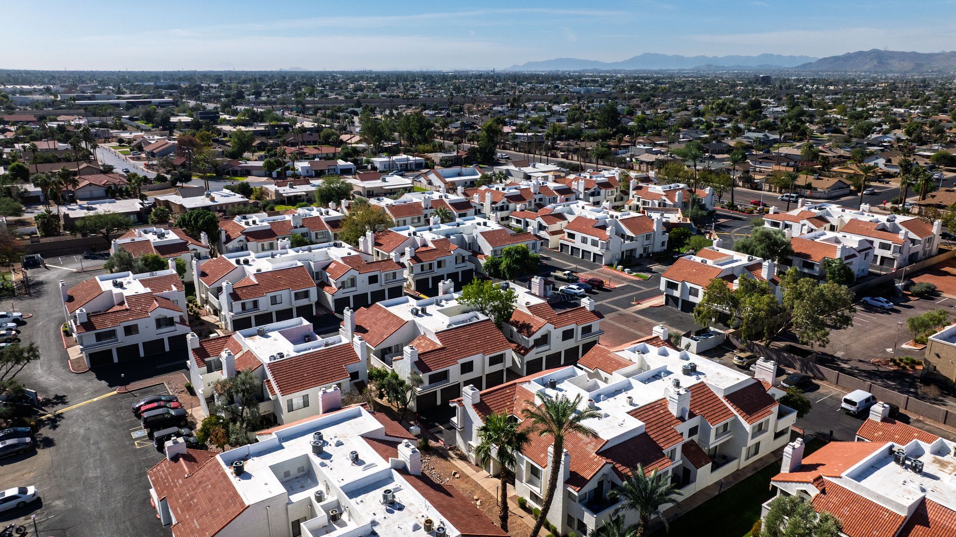 Aerial view of a suburban neighborhood with white buildings, red tile roofs, and green trees under a clear blue sky. Find convenient Tempe AZ apartment rentals at Talavera Apartments today.
