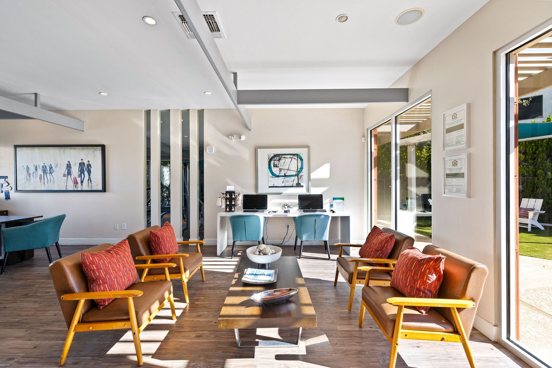 Reception area with brown leather chairs, red pillows, wood table, and two computer workstations.