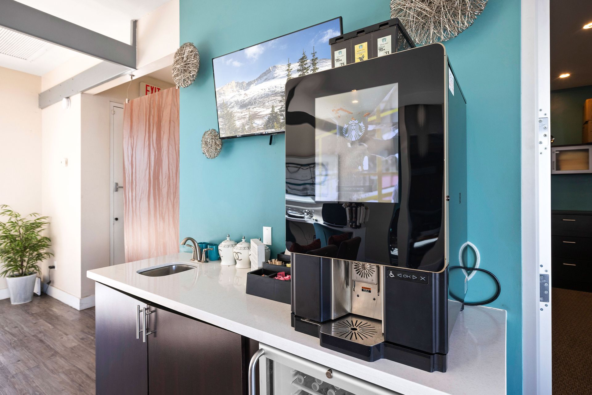 Coffee machine on a countertop against a teal wall with a TV and decorative spheres. Talavera Apartments offers connected downtown Tempe apartments—see what’s nearby.