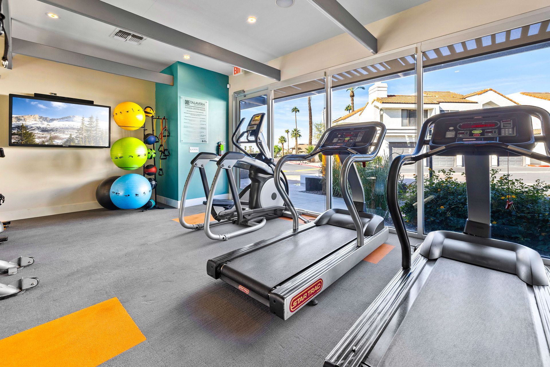 Gym interior with treadmills, elliptical, exercise balls, and a TV. Bright space with a view. Talavera Apartments showcases modern apartment homes in Tempe AZ—take a look.