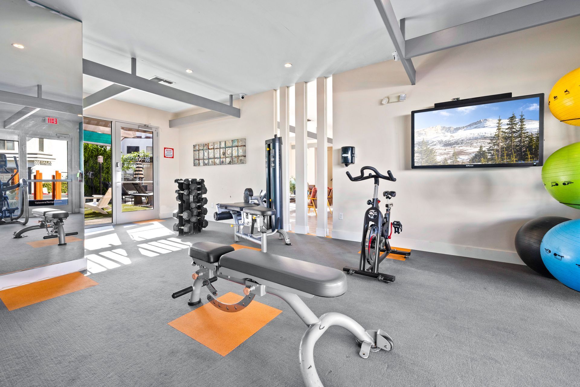 Gym with weight bench, equipment, TV, colorful exercise balls. Explore thoughtfully designed 1 bedroom apartments in Tempe AZ at Talavera Apartments.