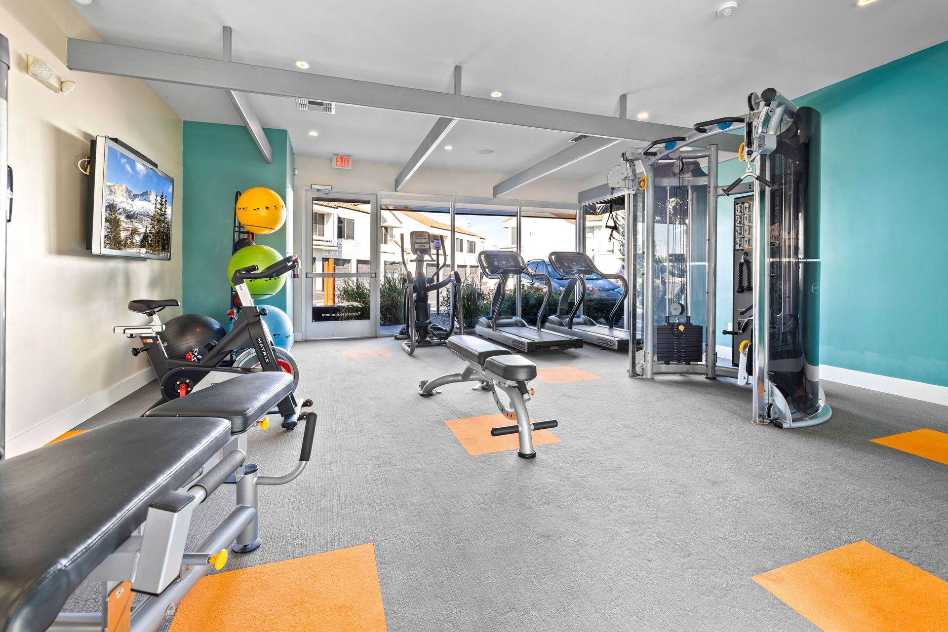 Gym with various exercise equipment: treadmills, weights, and benches. Turquoise and neutral-toned walls. Enjoy a relaxed pet-friendly community at Talavera Apartments—learn more.