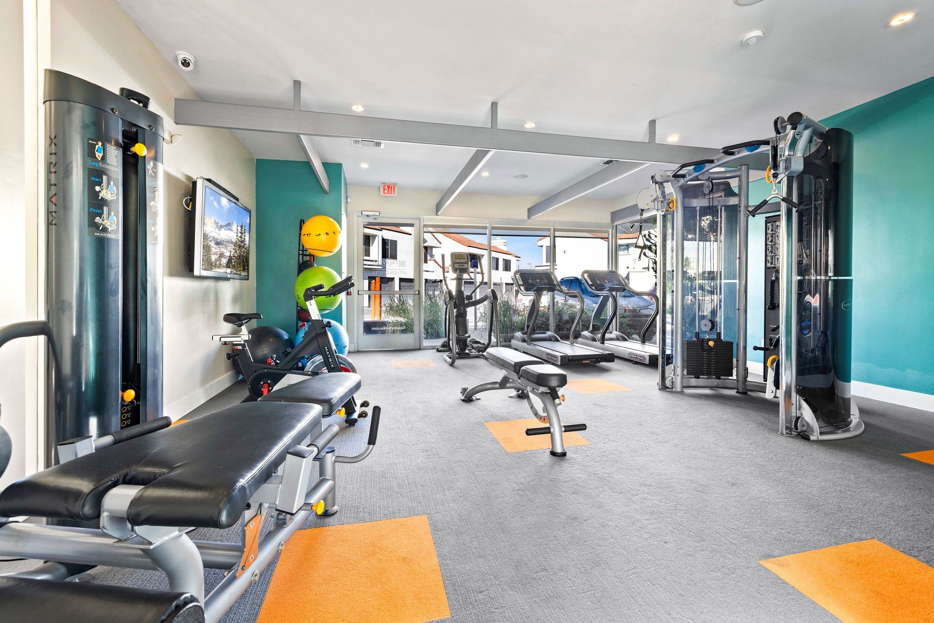 Gym with various exercise machines, turquoise walls, and gray floor with orange accents. Talavera Apartments features comfortable Tempe AZ rentals—explore your options.