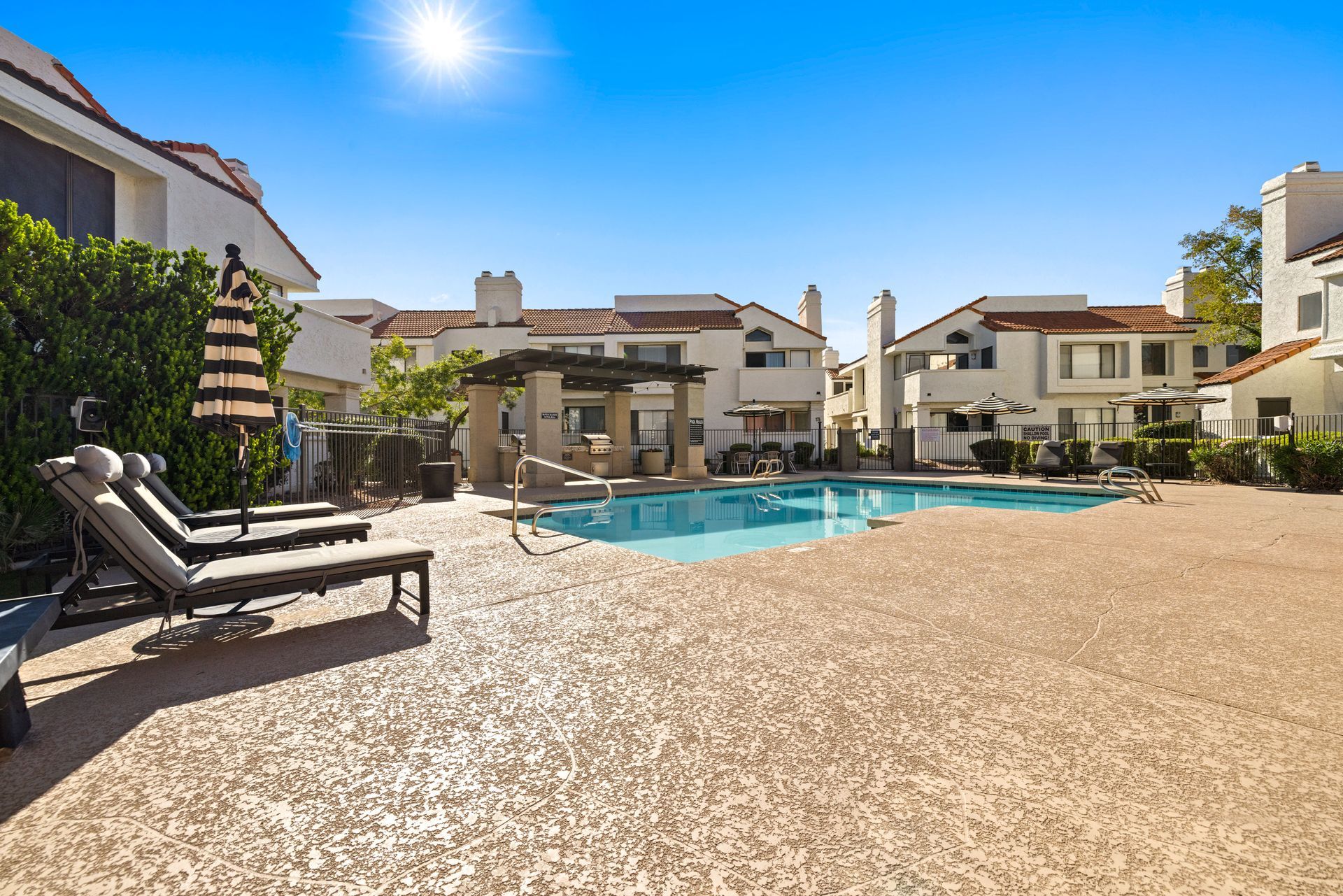 Swimming pool in a courtyard with lounge chairs. Buildings and a sunny sky are in the background. Live comfortably in a pet-friendly community at Talavera Apartments—discover more.
