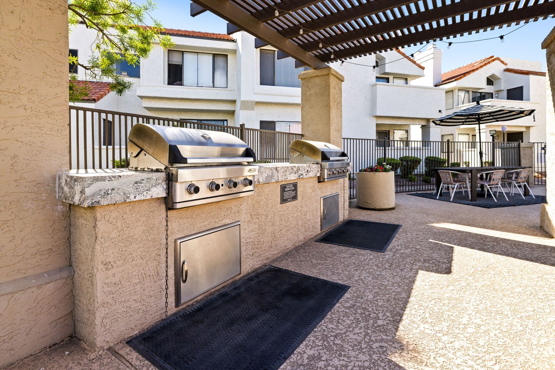 Outdoor grilling station with two stainless steel grills, a seating area, and a pergola overhead. Talavera Apartments showcases upscale apartments in Tempe AZ—learn more.