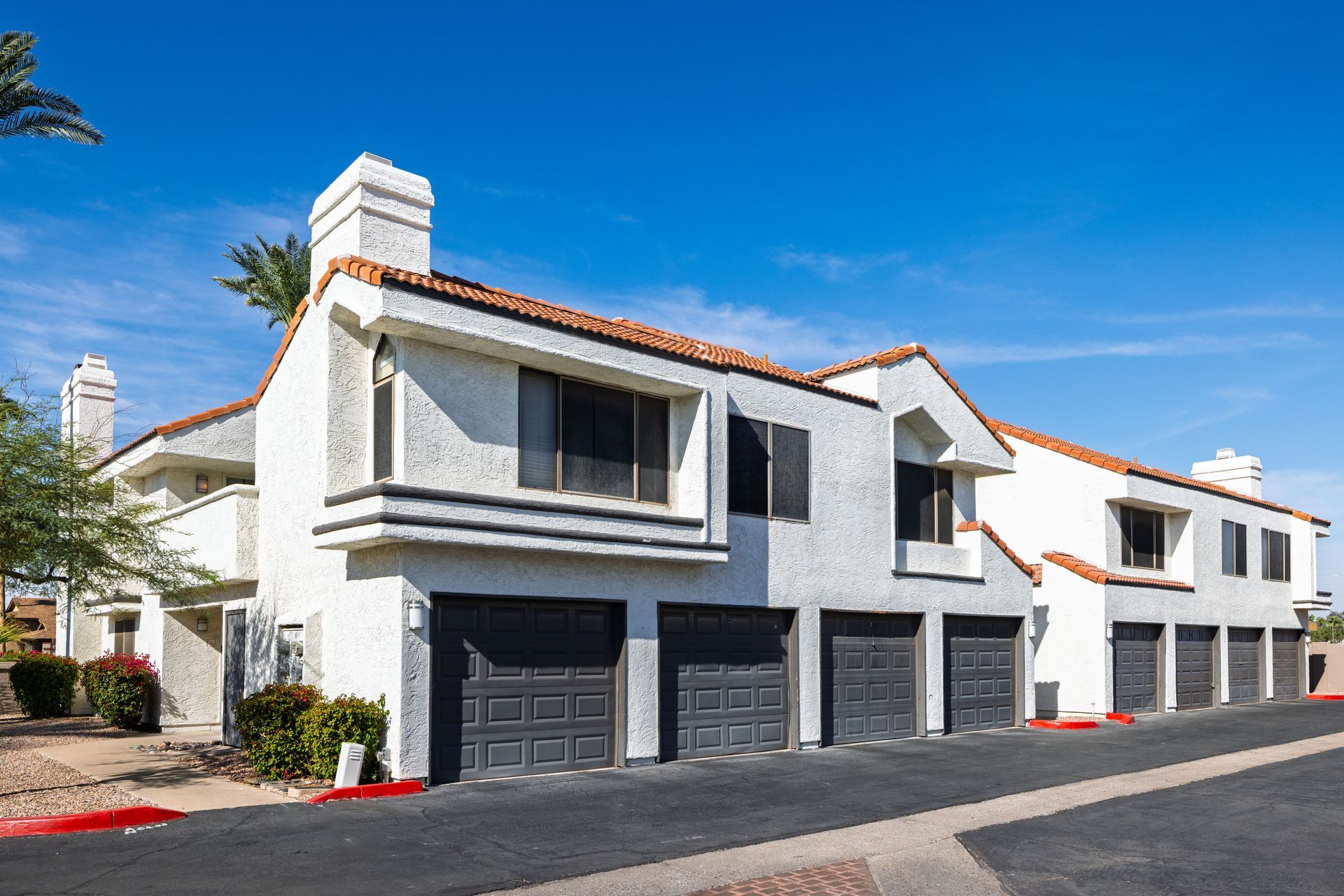 White stucco apartment building with dark garage doors under a clear blue sky. Talavera Apartments places you near it all with downtown Tempe apartments.