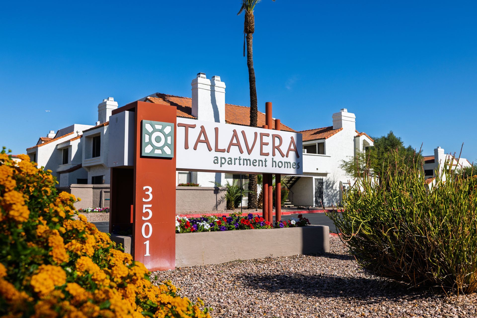 Sign for Talavera apartment homes, with address 3501, in front of white stucco buildings with terra cotta tile roofs. Discover comfortable Tempe AZ apartment rentals at Talavera Apartments today.