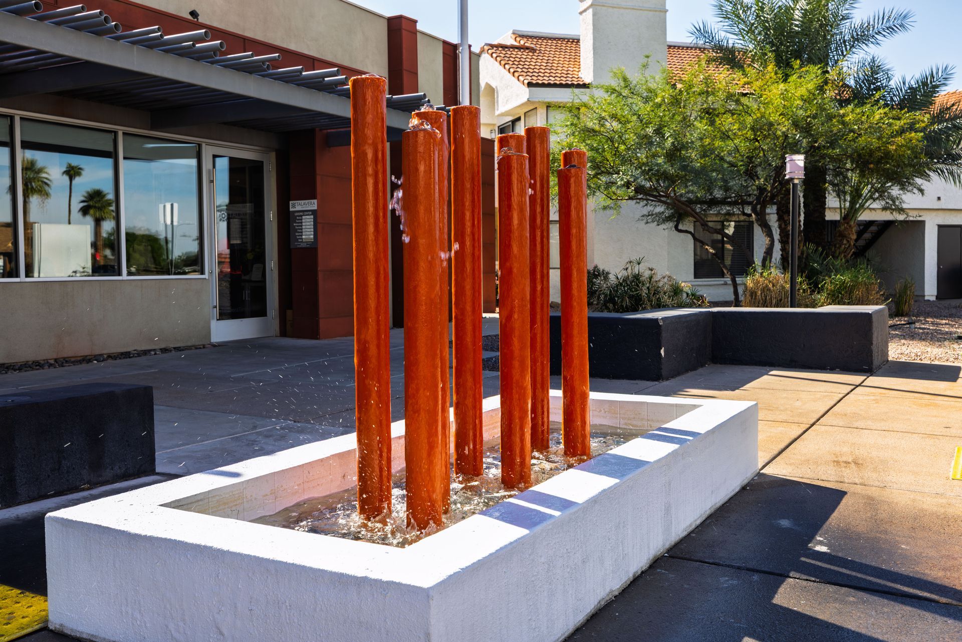 Fountain with vertical, brown water features in a white concrete basin, outside a building with glass windows. Talavera Apartments highlights modern pet-friendly apartments in Tempe AZ.