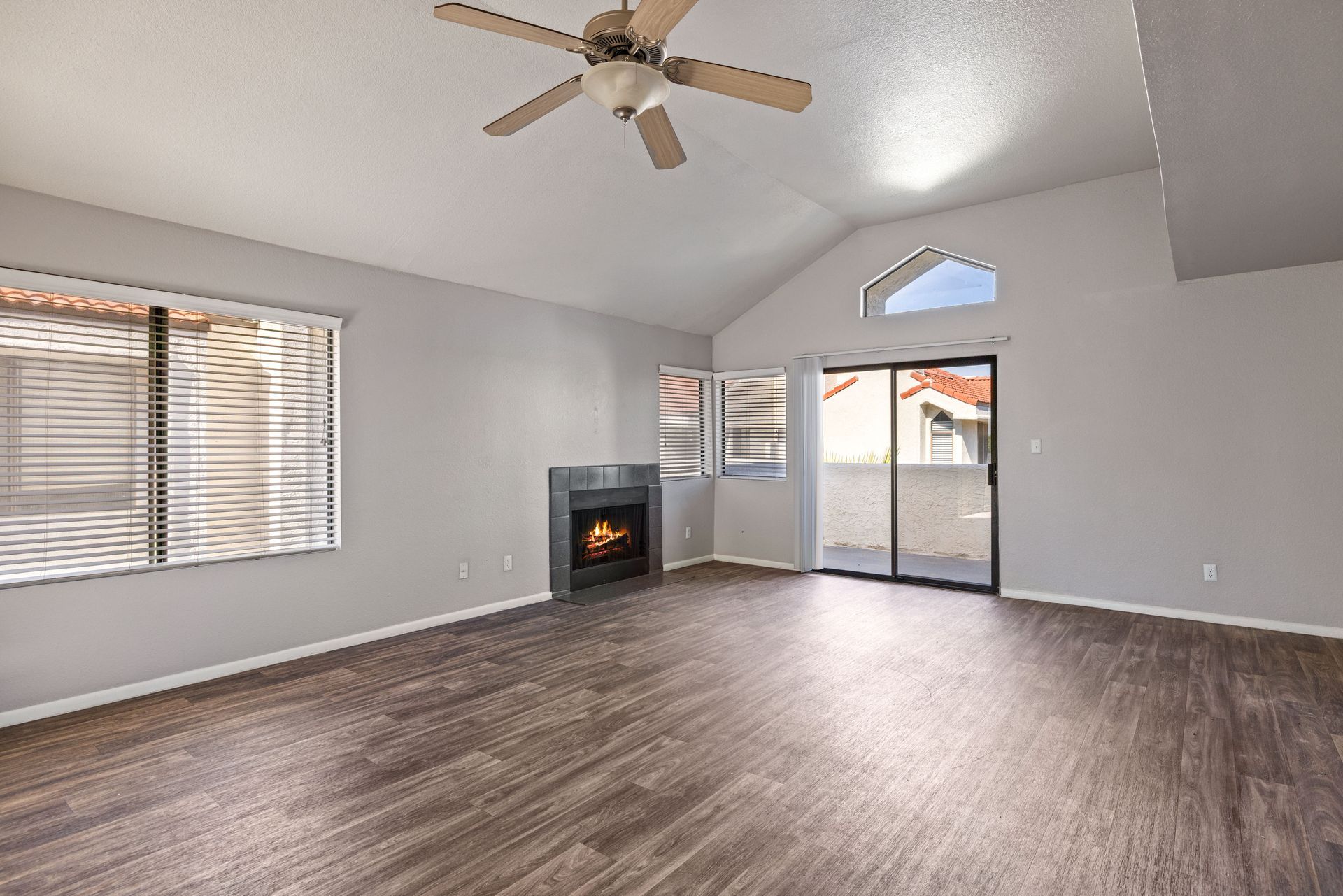 Living room with fireplace, sliding glass door, and ceiling fan. Light gray walls, dark wood floor. Find your space in 1 bedroom apartments in Tempe AZ at Talavera Apartments.