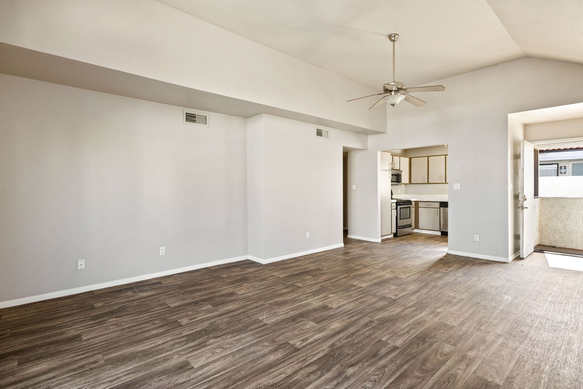 Empty living room with wood-look flooring, light gray walls, and an open doorway to the kitchen. Talavera Apartments showcases pet-friendly apartments in Tempe AZ—explore the options.