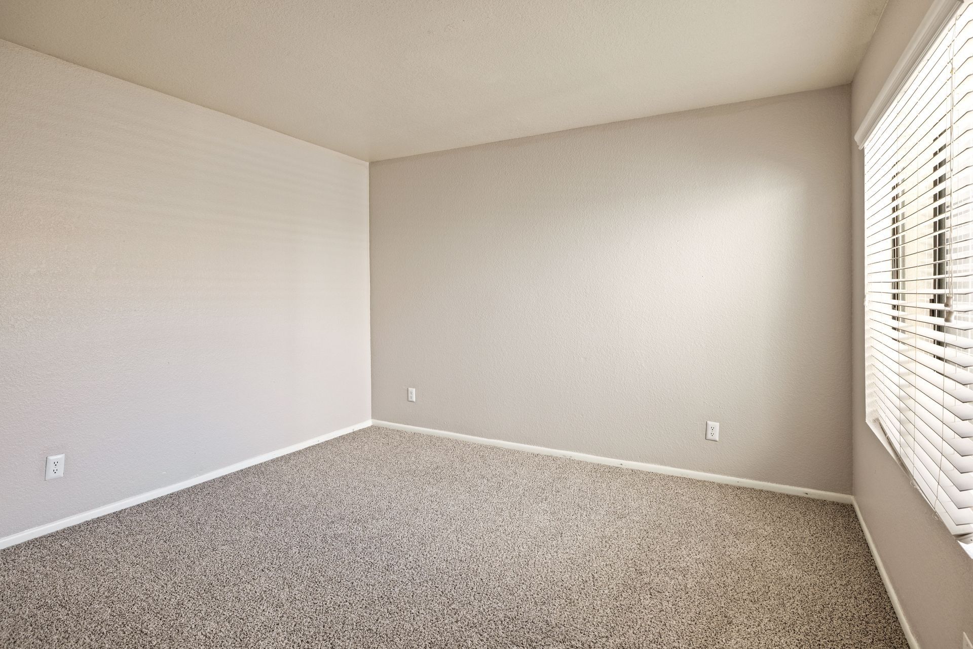 Empty room with beige walls, patterned carpet, and a window with blinds. Talavera Apartments highlights upscale apartments in Tempe AZ—discover your fit.