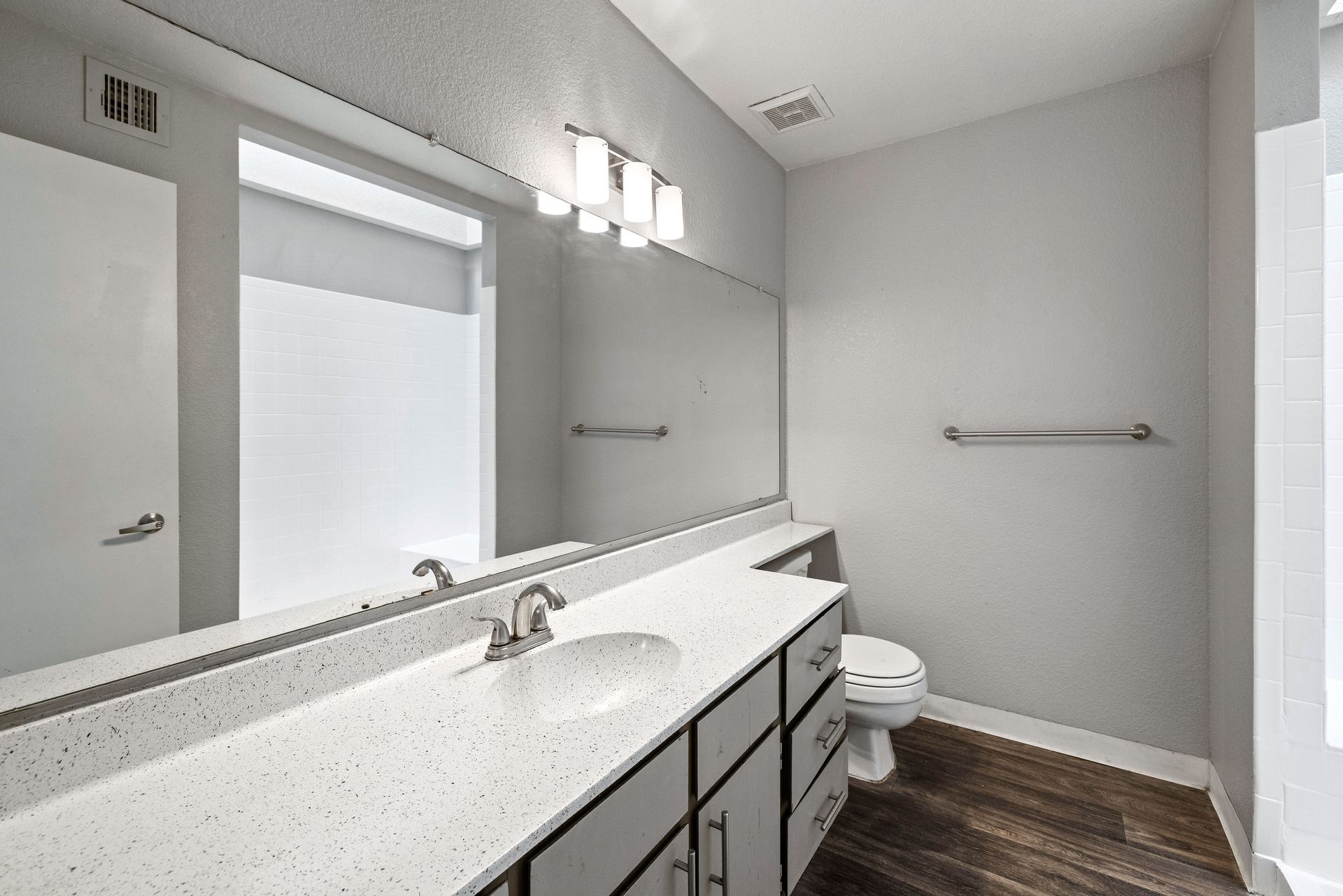 Bathroom with white countertop, large mirror, and three-light fixture over a vanity with a sink and cabinets. Live comfortably in a pet-friendly community at Talavera Apartments—check it out.