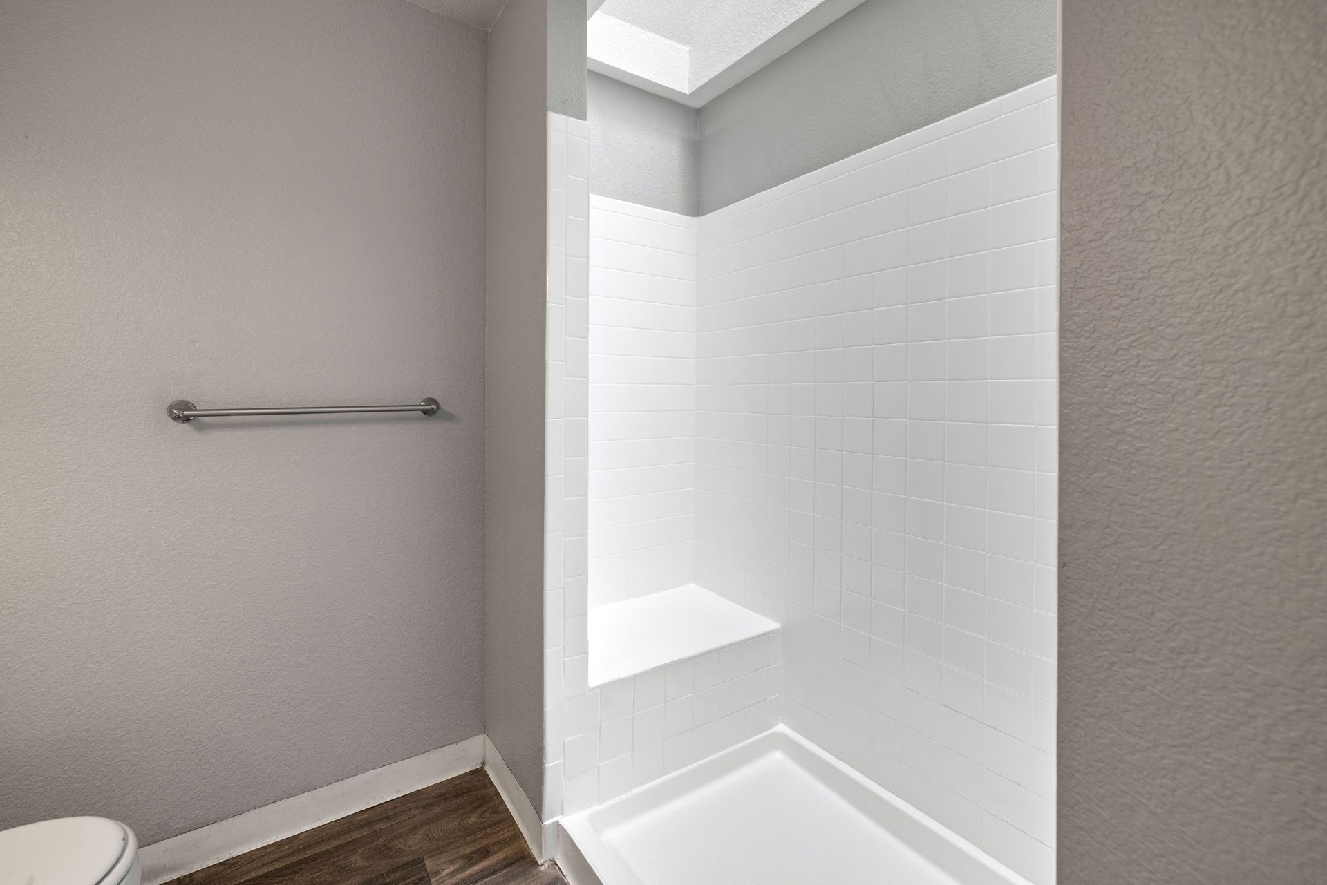 Bathroom with white tiled shower, built-in seat, and a skylight. A towel bar hangs on the left wall. Talavera Apartments provides stylish apartment homes in Tempe AZ—explore today.