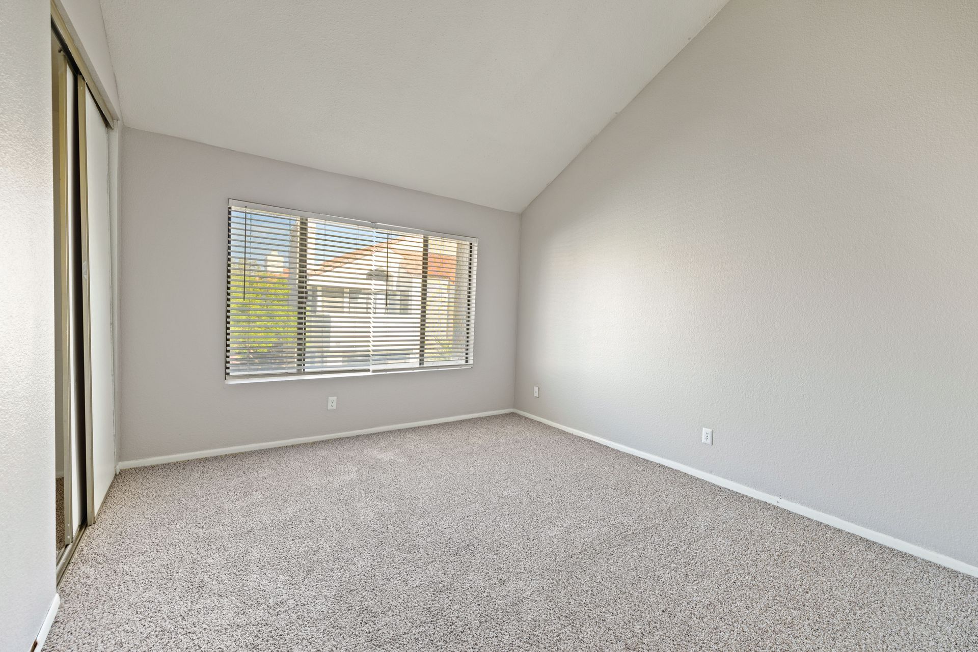 Empty room with neutral walls, carpet, window with blinds, and sliding door. Talavera Apartments offers thoughtfully designed Tempe AZ rentals—take a look.