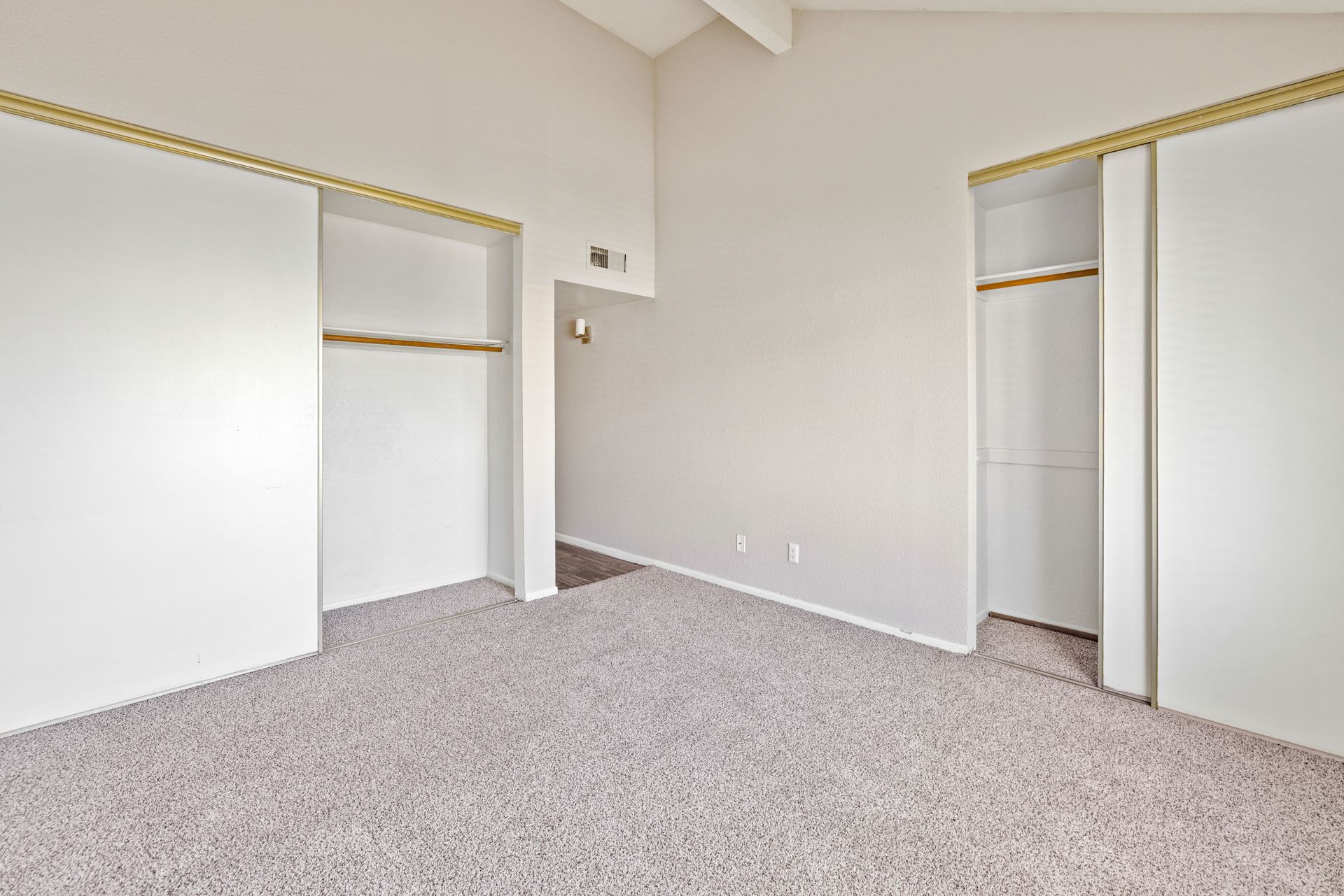 Empty bedroom with beige carpet, white walls, and two sliding closet doors. Discover spacious 2 bedroom apartments in Tempe AZ at Talavera Apartments.