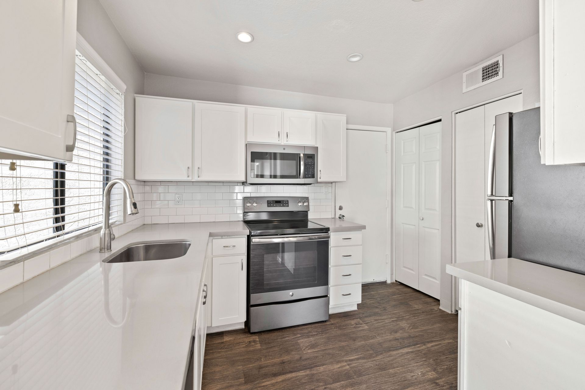 White kitchen with stainless steel appliances, cabinets, and a window with blinds. Talavera Apartments features stylish 2 bedroom apartments in Tempe AZ—learn more today.