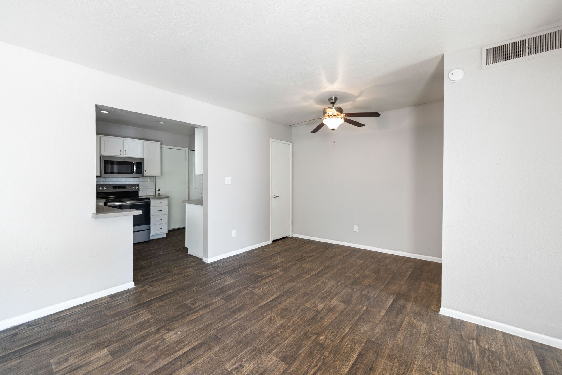 Empty living room with wood-look flooring, light gray walls, and an open kitchen view. Explore pet-friendly apartments in Tempe AZ at Talavera Apartments today.