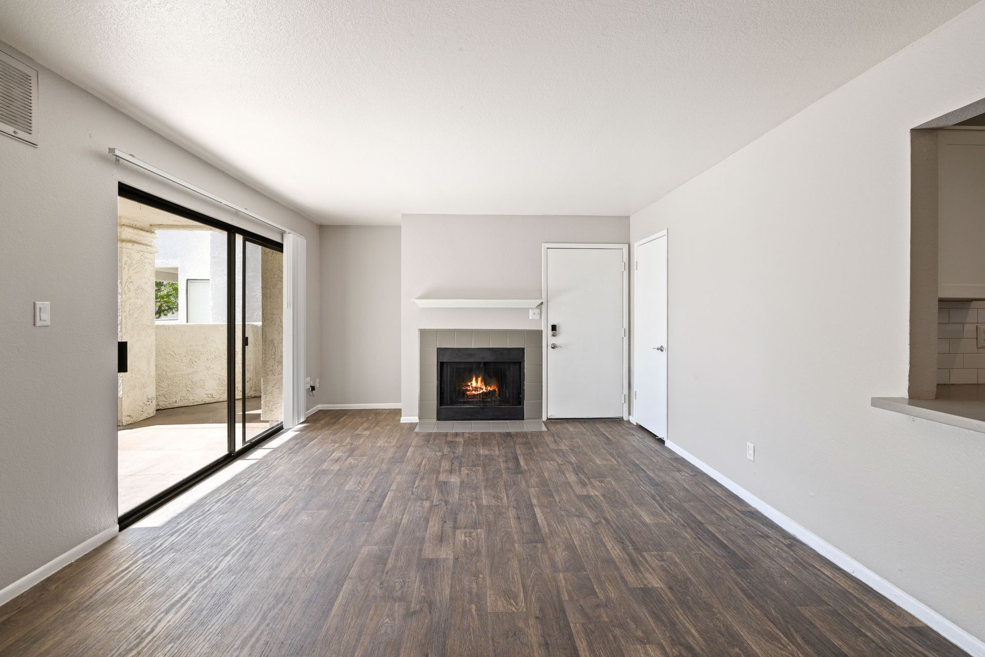 Empty living room with fireplace, sliding door to patio, and wood flooring. Talavera Apartments offers inviting 1 bedroom apartments in Tempe AZ—discover more.