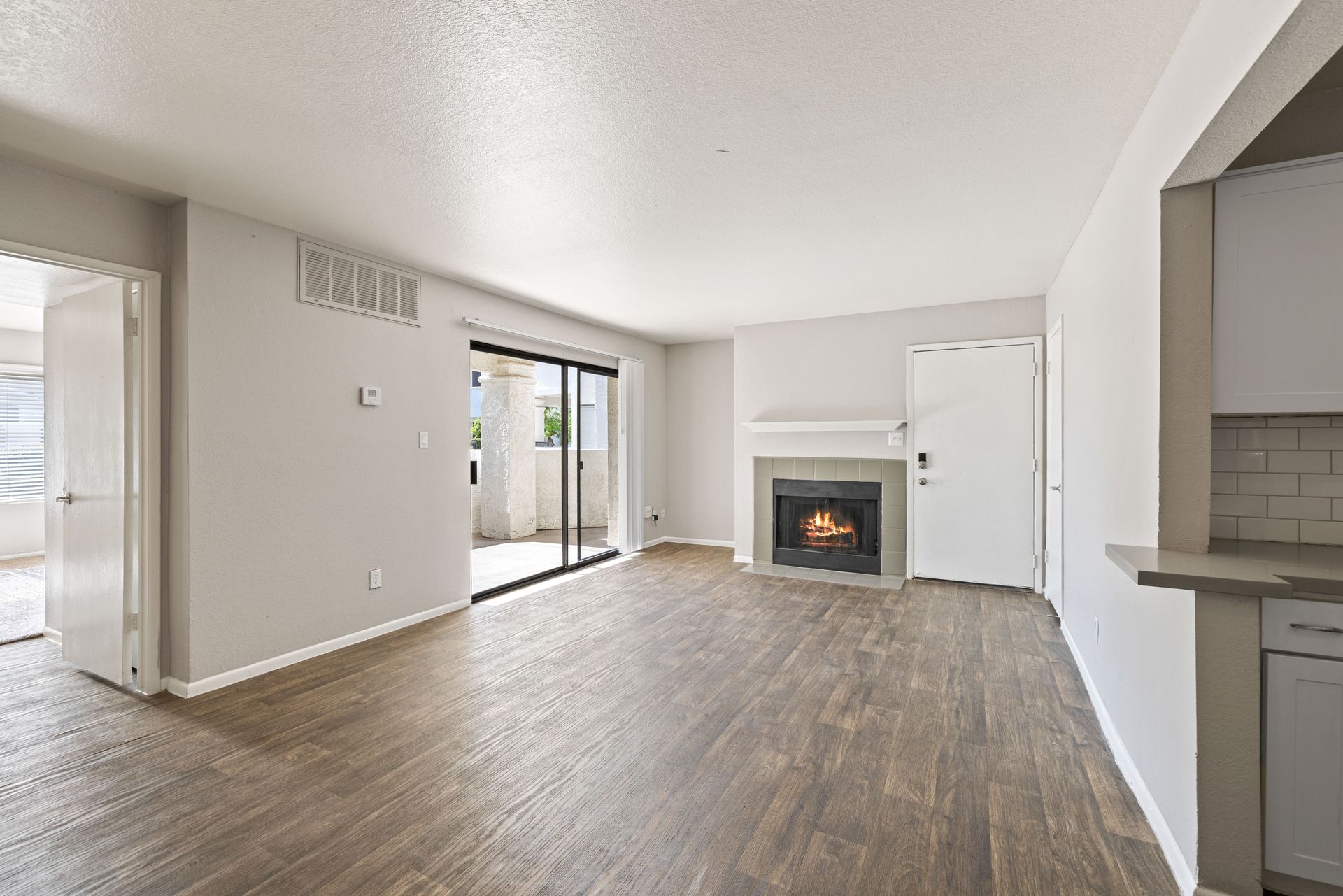 Empty living room with fireplace, sliding glass door to balcony, and kitchen opening. Talavera Apartments provides convenient Tempe AZ apartment rentals—check them out.