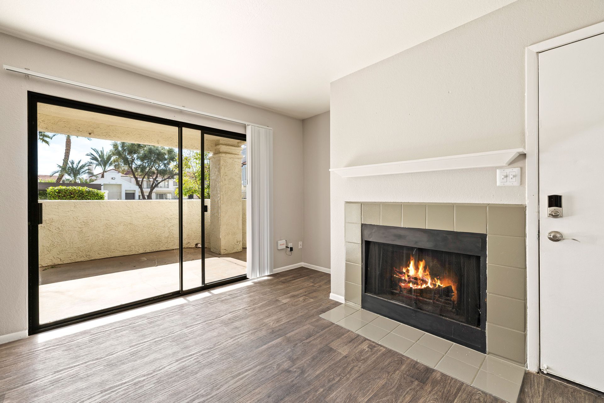 Living room with fireplace and sliding door to balcony. Dark wood floors, light walls. Modern apartments in Tempe AZ await at Talavera Apartments—schedule a visit.